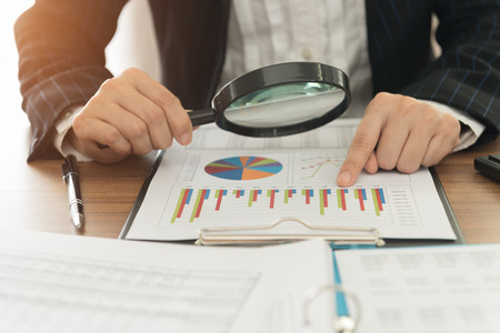 Business analyst using magnifying to review financial graphs. Concept of Analyze return on investment and business analytics growth.の写真素材