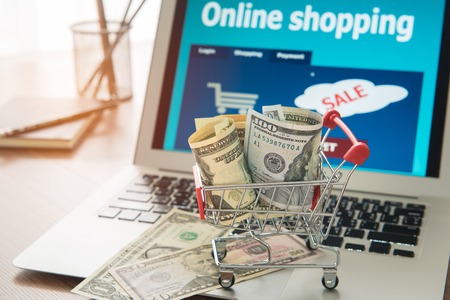 Online shopping. Dollar banknotes and shopping carts on a laptop. E-commerce business and modern lifestyle concept.の写真素材