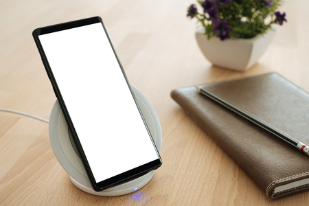 Mobile smartphone is placed on a wireless fast charger. Blank screen with clipping path on screen for your advertising.の写真素材