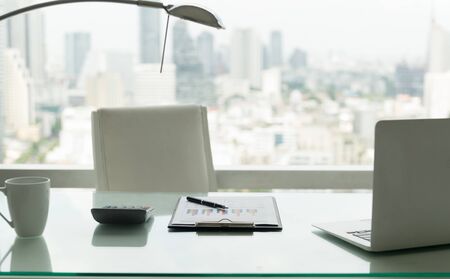 Office workplace with notebook laptop, financial report, calculator on work desk in office with city view.の写真素材