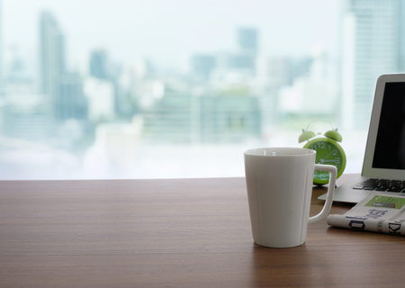 Coffee, newspapers, alarm clocks and laptop are placed on the table by the window against the...