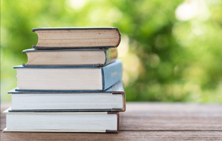 A stack of old books on a wooden table with natural bokeh background. Book concept of education