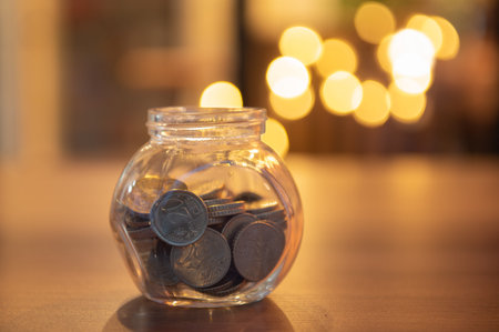 A coin in a glass jar placed on the desk against a bokeh background. Finance and saving money...