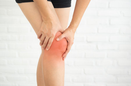 Woman holding her painful knee. Red around the knee pain area. The concept of healthcare and medicine.の写真素材