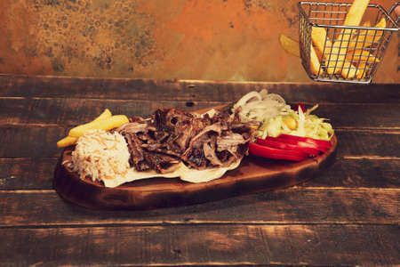Doner kebab is lying on the cutting board. Shawarma with meat, onions, salad lies on a dark old wooden tableの写真素材