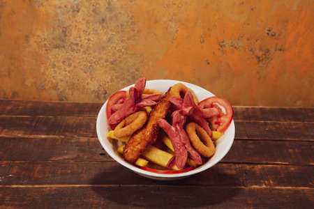 Delicious snack plate, french fries, onion rings, spring rolls or sausages on the tableの写真素材