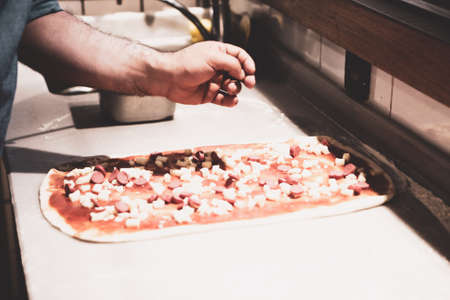 Pizza chef put sauce on base in a commercial kitchenの写真素材