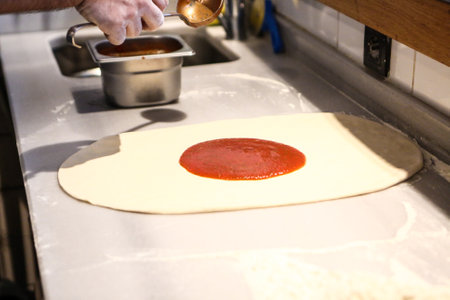 Pizza chef put sauce on base in a commercial kitchenの写真素材