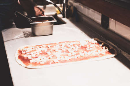 Pizza chef put sauce on base in a commercial kitchenの写真素材