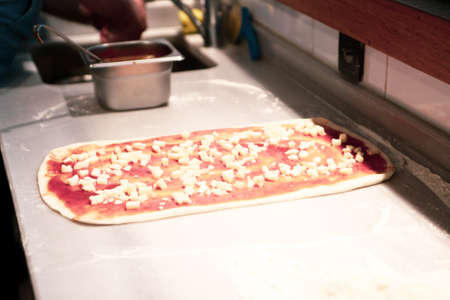 Pizza chef put sauce on base in a commercial kitchenの写真素材