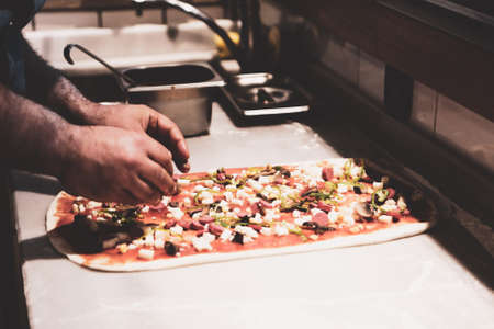 Pizza chef put sauce on base in a commercial kitchenの写真素材
