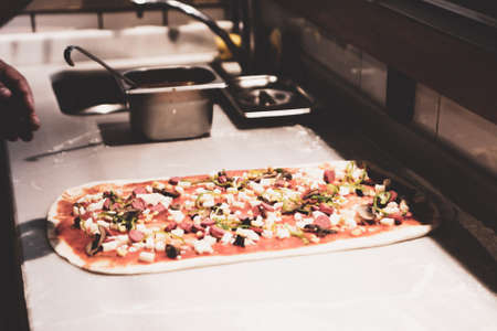 Pizza chef put sauce on base in a commercial kitchenの写真素材