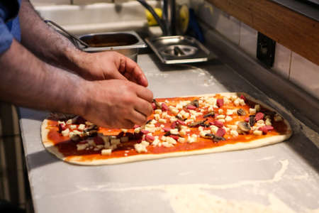 Pizza chef put sauce on base in a commercial kitchenの写真素材