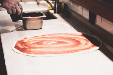 Pizza chef put sauce on base in a commercial kitchenの写真素材
