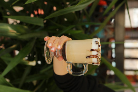 Iced coffee with milk. Iced coffee latte. Woman holding glass cup of iced coffee.