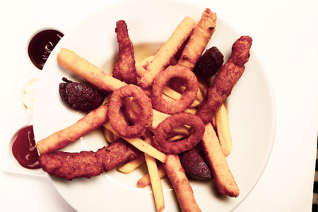 Delicious snack plate, french fries, onion rings, spring rolls or sausages on the table