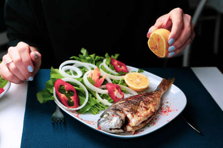 Fried sea bream (cupra) fish on white plate with onion, garden rocket and lemon slicesの写真素材