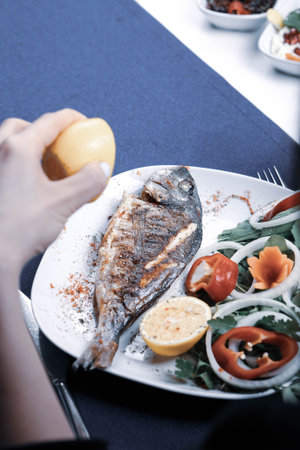 Fried sea bream (cupra) fish on white plate with onion, garden rocket and lemon slicesの写真素材