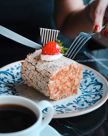 A piece of cake with strawberries and a cup of coffee on the tableの写真素材