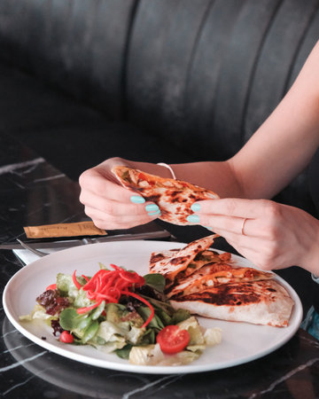 Female hands hold a piece of pizza on a plate in a restaurant