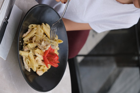 Woman eating pasta with vegetables on table in cafe, closeupの写真素材