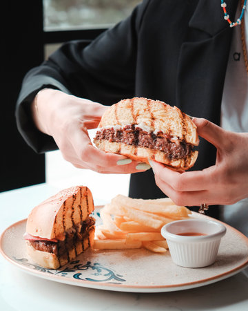 Cropped image of woman holding hamburger with french fries on tableの写真素材
