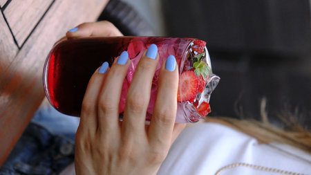 Woman's hand with blue manicure holds a glass of strawberry smoothie.の写真素材