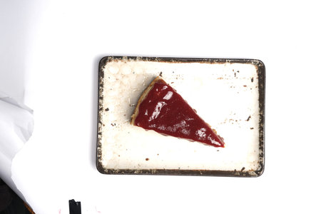 A piece of cheesecake with strawberry jam on a white background.