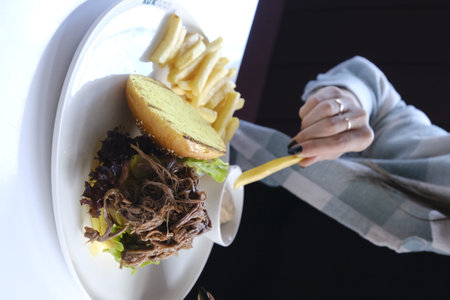 Woman eating hamburger and french fries on white plate.の写真素材