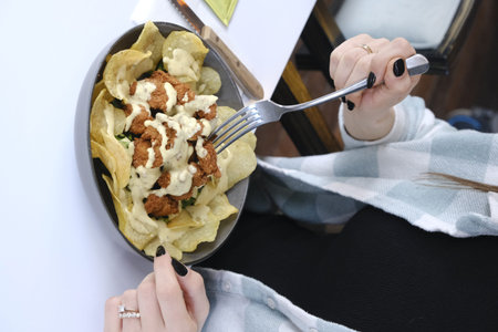 Woman eating nachos with mayonnaise in a restaurant.