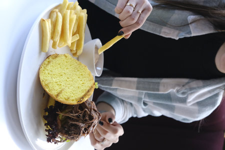 Woman eating hamburger and french fries. Close-up, top view.の写真素材
