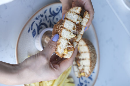 Hands holding a sandwich with chicken, cheese and fries.