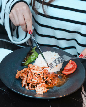 Close-up of woman's hand with red manicure holding fork and knife on plate with rice.の写真素材