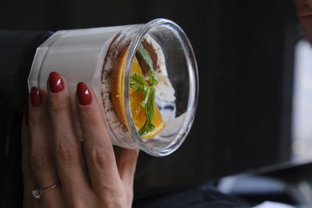 Woman's hand holding a glass of chocolate mousse with orange and mint
