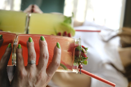 Close-up of woman's hand with green manicure holding a glass of cocktailの写真素材