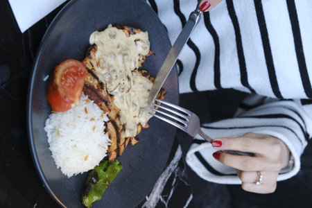 Woman eating rice with tomato and mushroom in black plateの写真素材