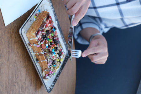 Closeup of woman eating waffle with whipped cream and candies
