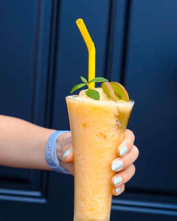 Fruit smoothie in woman's hand on a blue background.の写真素材