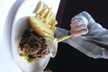 Hands of woman eating hamburger and french fries in restaurant.の写真素材