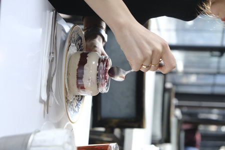 Close-up of a woman's hand holding a spoon and scooping a jar of blueberry jamの写真素材