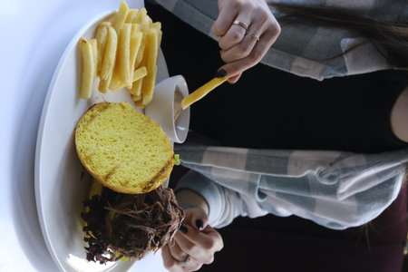 Woman eating a hamburger and french fries. Close-up.の写真素材
