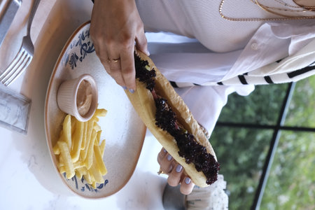 Woman eating a hot dog with black currant jam and french friesの写真素材