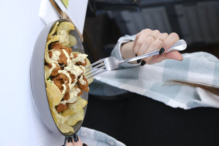 Woman's hand holding a fork with fast food on the table.の写真素材