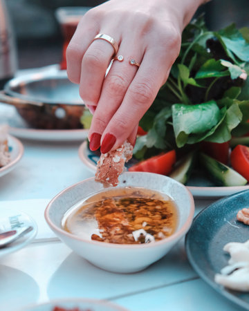 Close-up of a woman's hand holding a slice of bacon in a bowl of soupの写真素材