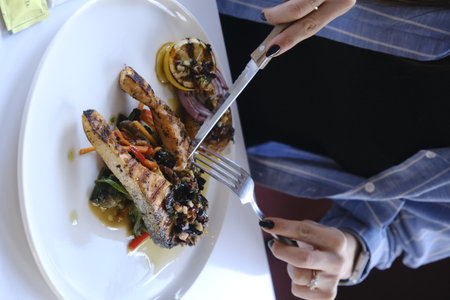 Woman eating fish and vegetables on a white plate in a restaurant.の写真素材