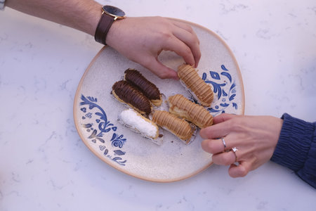 Man and woman hands holding chocolate eclairs on a plate.