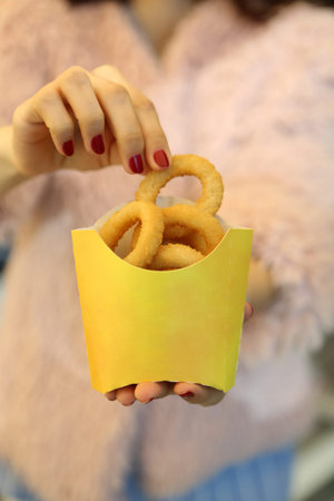 Woman holding tasty onion rings in paper box, closeup of hands