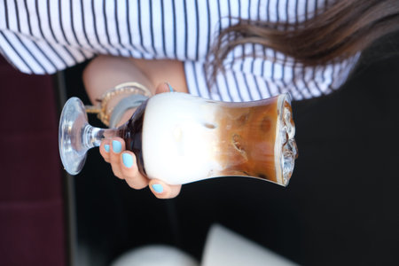 Woman holding a glass of cappuccino coffee, closeup