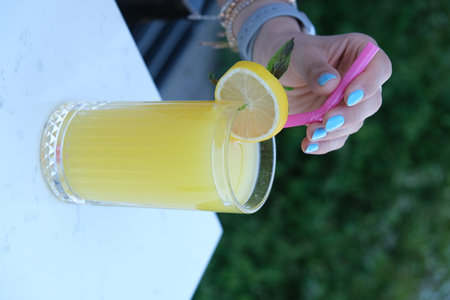 Female hand with blue nail polish holding a glass of fresh lemonadeの写真素材