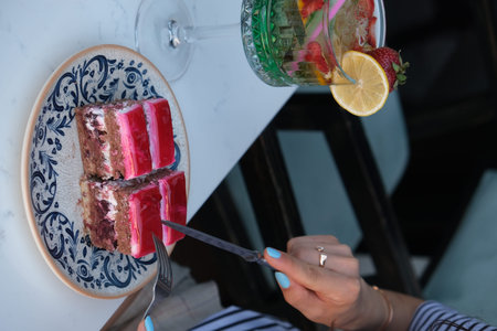 Close-up of a woman's hand holding a knife and cutting a piece of cake on a plate